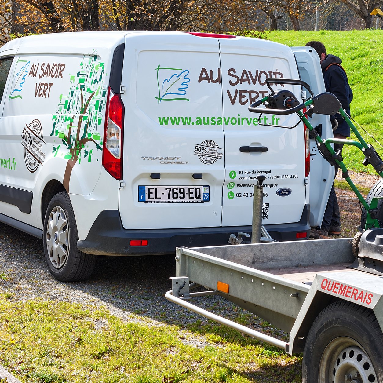 Camionnette Au Savoir Vert garée sur l’herbe, avec une tondeuse et une remorque, pour l’entretien d’espaces verts.