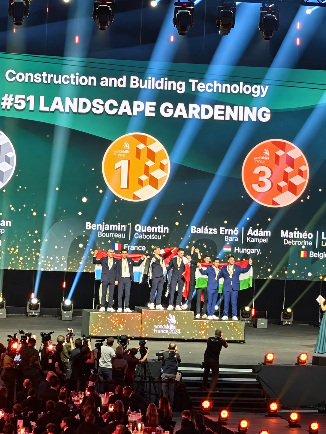 Podium de la catégorie Landscape Gardening : l’équipe de France médaillée d’or sous les projecteurs, devant un écran géant et le public.